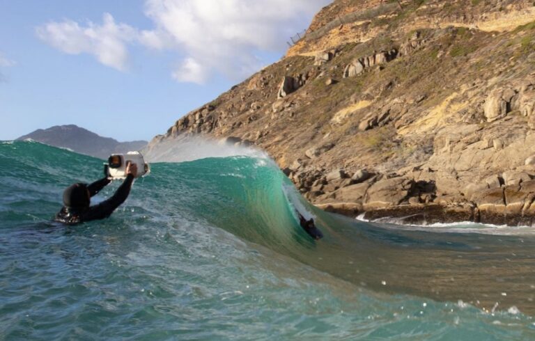 James Symmonds underwater filming a surfer, capturing dynamic action in ocean waves.
